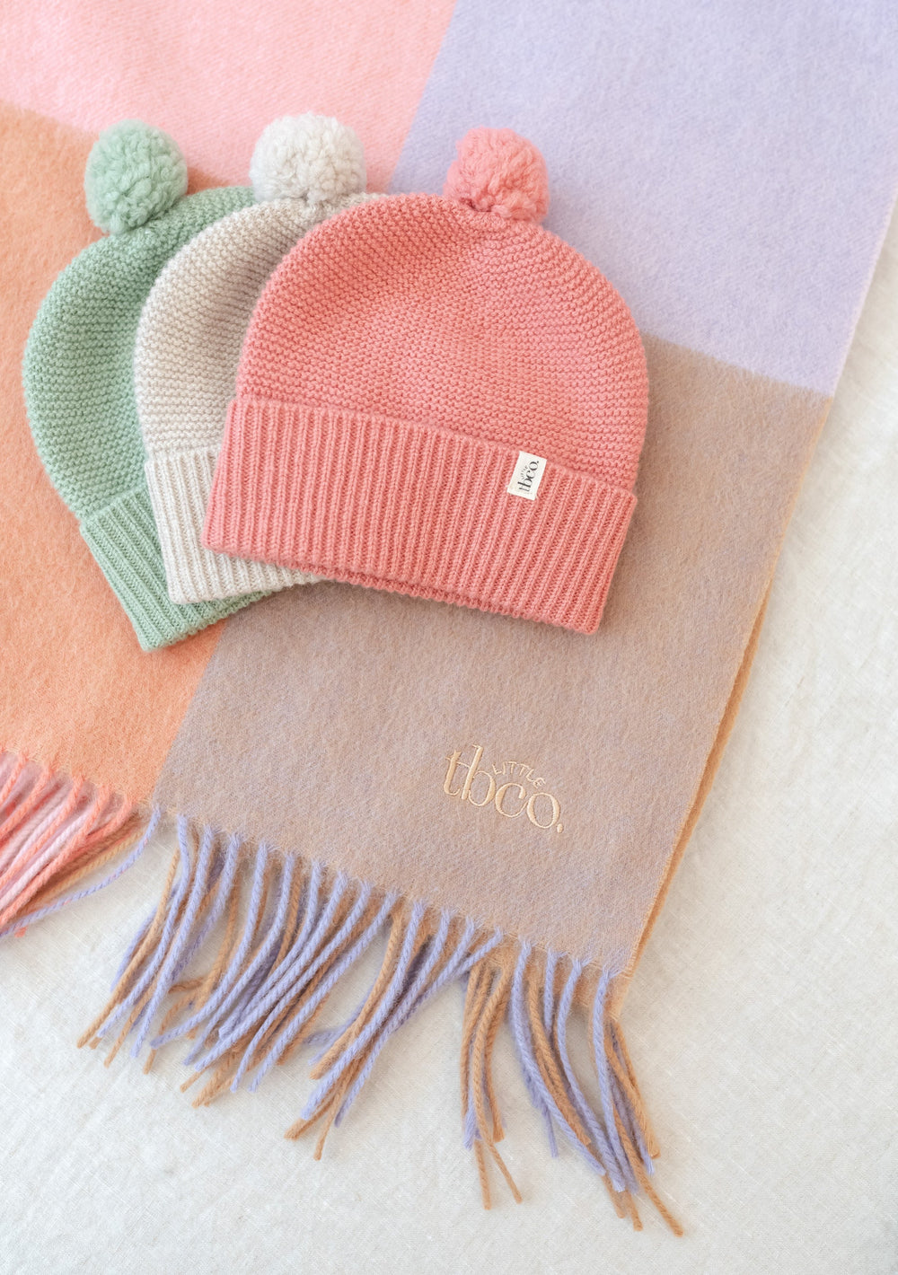 TBCo Merino Wool Baby Beanie in Rose with pom-pom detail, knitted in soft pink wool, displayed with mint and cream beanies