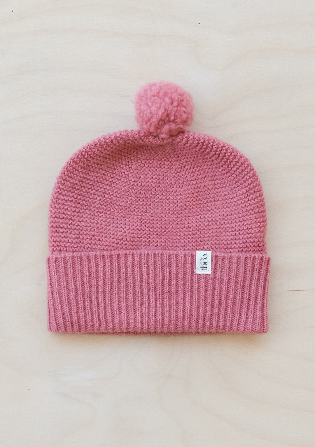 TBCo Merino Wool Baby Beanie in Rose with pom pom detail, featuring ribbed cuff and knitted texture in soft pink colour