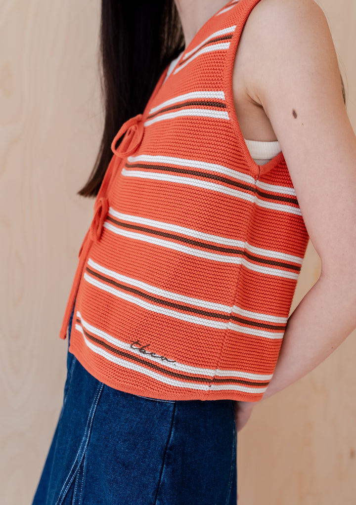 TBCo Cotton Knitted Vest in Tangerine Stripe with white stripes and front ties, shown from side view against beige background