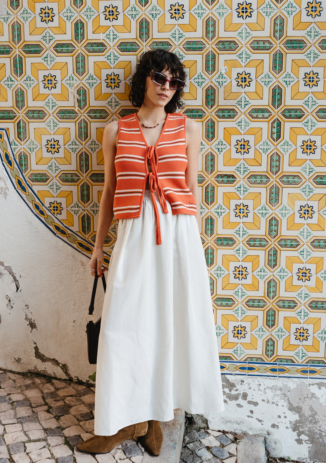 TBCo Cotton Knitted Vest in Tangerine Stripe styled with white maxi dress against geometric tiled wall background