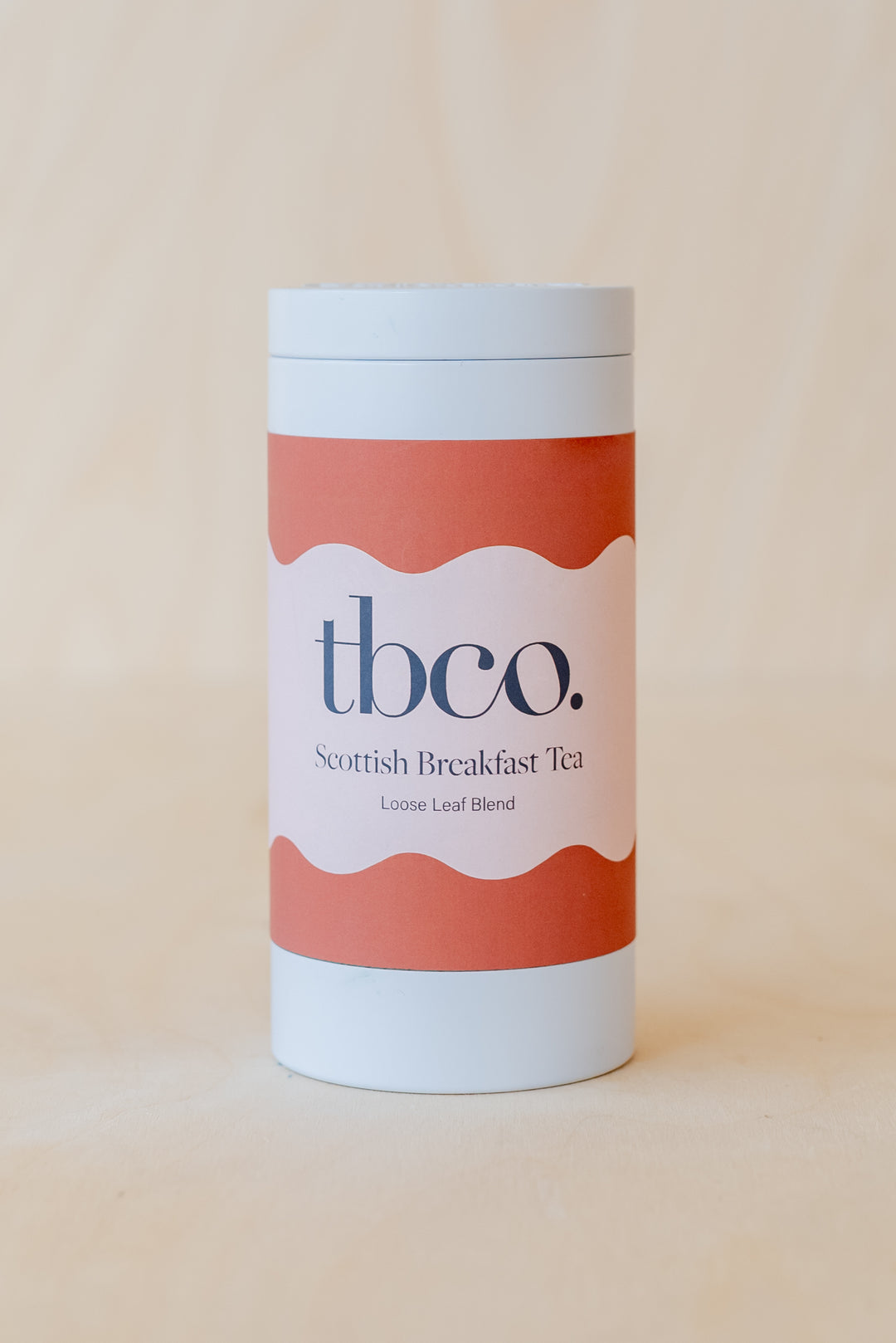 Cylindrical white and coral tea tin containing TBCo Scottish Breakfast Tea loose leaf blend, featuring minimalist wave design
