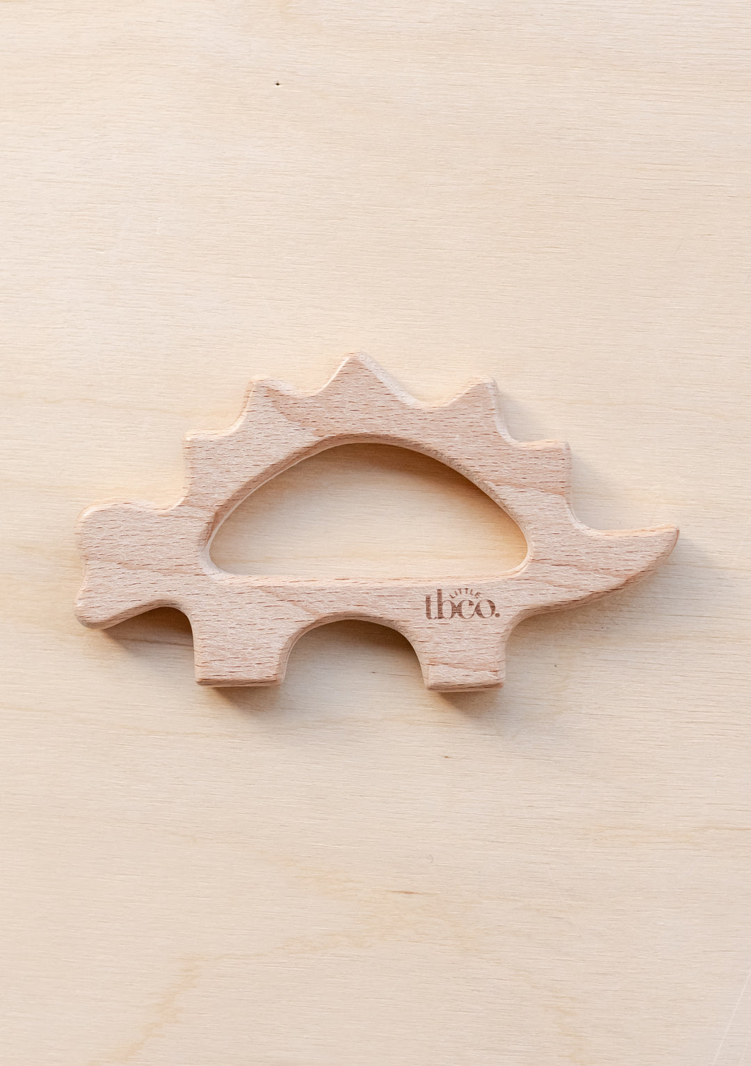 TBCo organic wooden dinosaur teether toy in natural beech wood, shaped like a stegosaurus with smooth curves and spikes