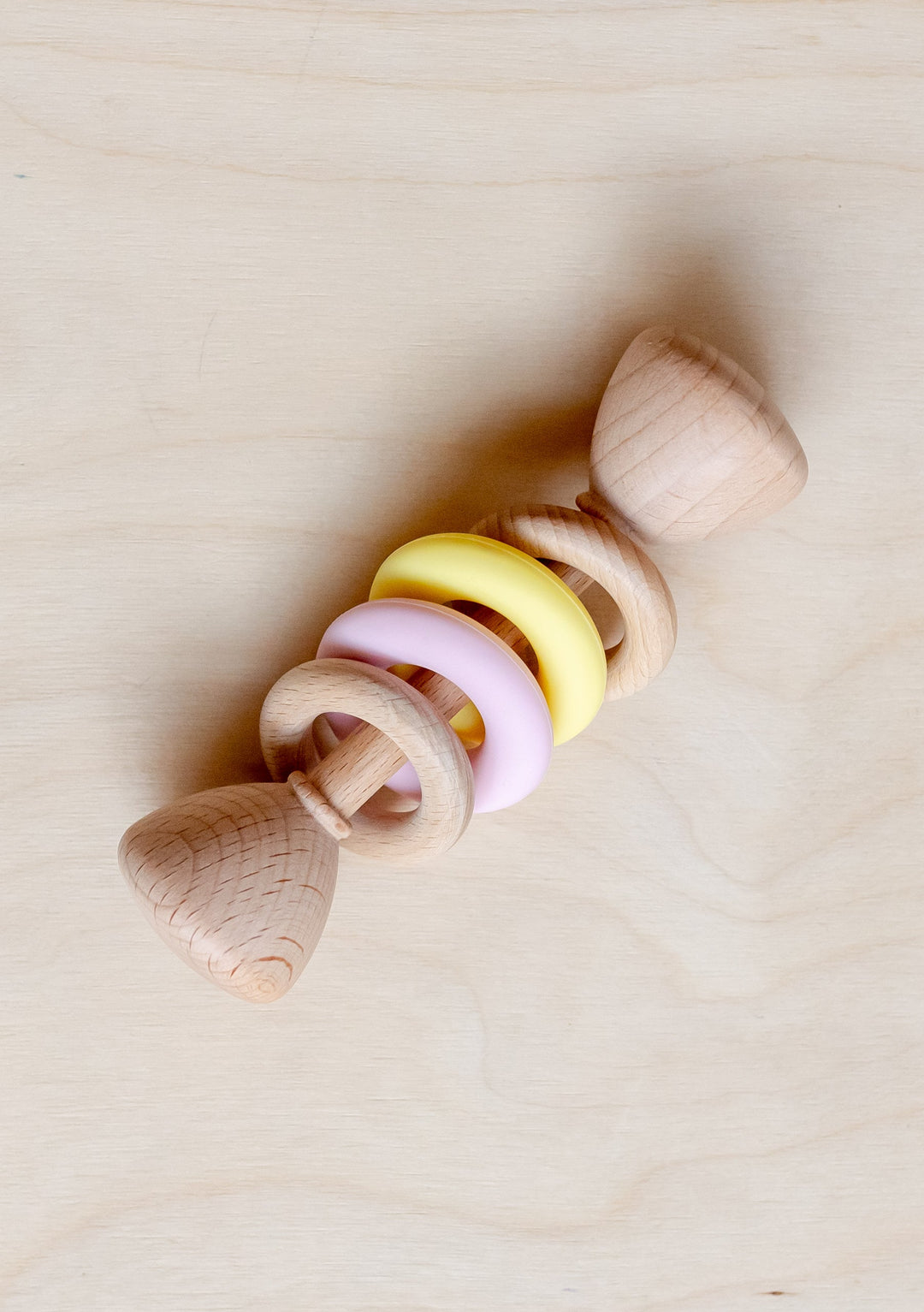 TBCo Organic Wooden Rattle Pink with yellow and pink rings, made from natural beech wood on light wooden background