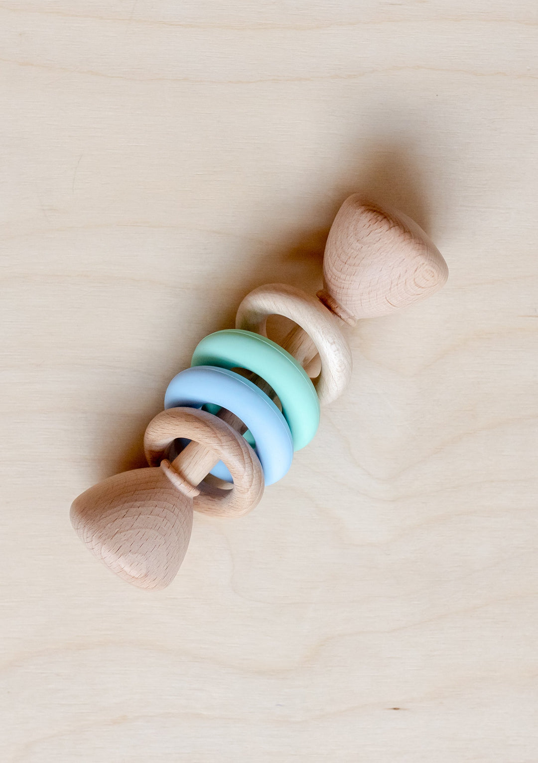 TBCo Organic Wooden Rattle Blue with mint and blue rings on natural beech wood, displayed on light wooden surface