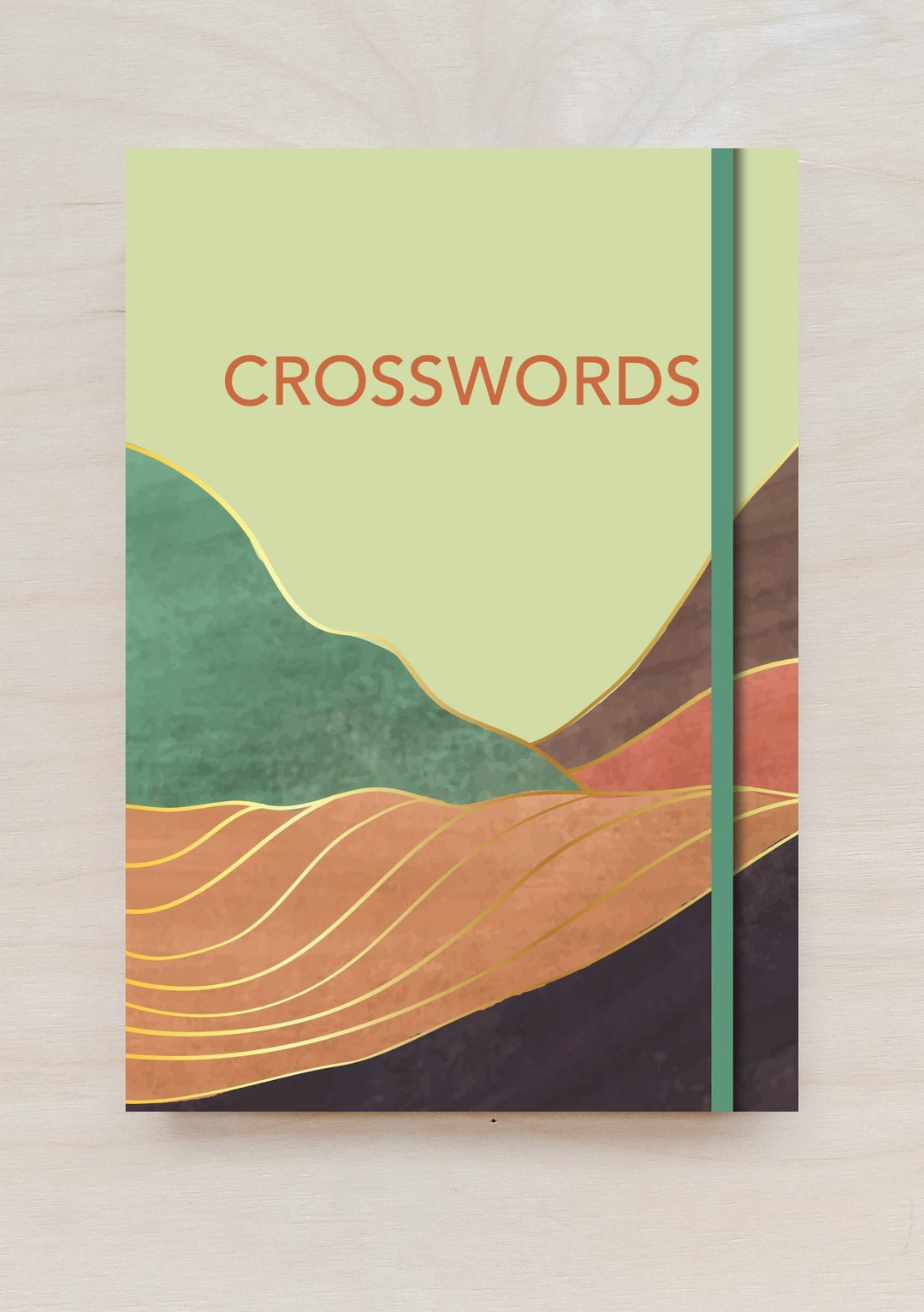 TBCo Crosswords Book with abstract mountain landscape design in green, orange and brown on pale yellow cover with elastic band