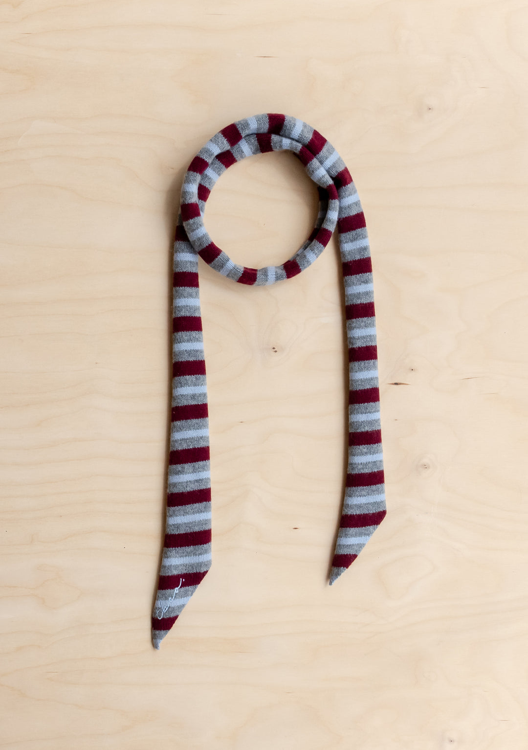 A TBCo Merino Wool Neck Tie in Burgundy Stripe lying flat on a wooden surface.