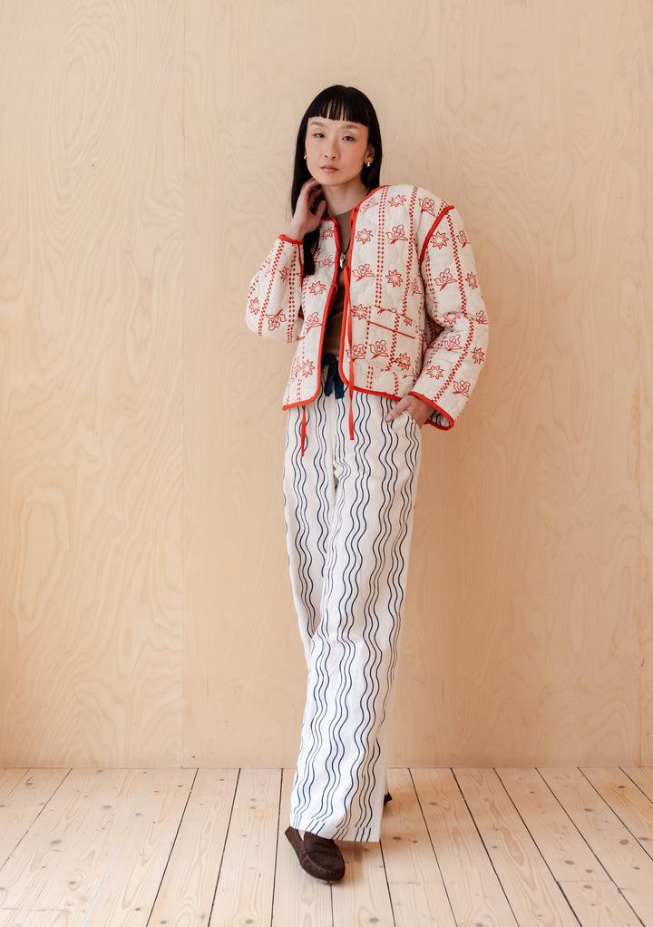 Person wearing TBCo Quilted Cotton Jacket in Reversible Flora Wave with navy wave-print trousers against beige background