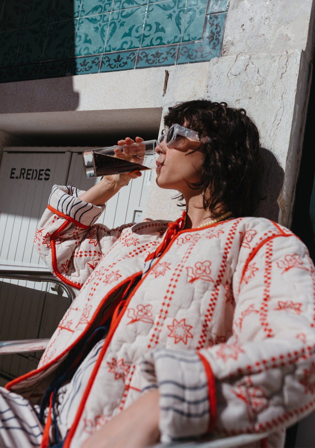 Model wearing TBCo reversible Quilted Cotton Jacket in Flora Wave pattern, featuring white and red quilted design with sunglasses