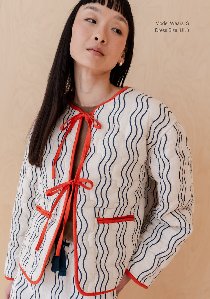 Model wearing TBCo Quilted Cotton Jacket in Reversible Flora Wave with navy wave pattern and red tie fastenings in size S