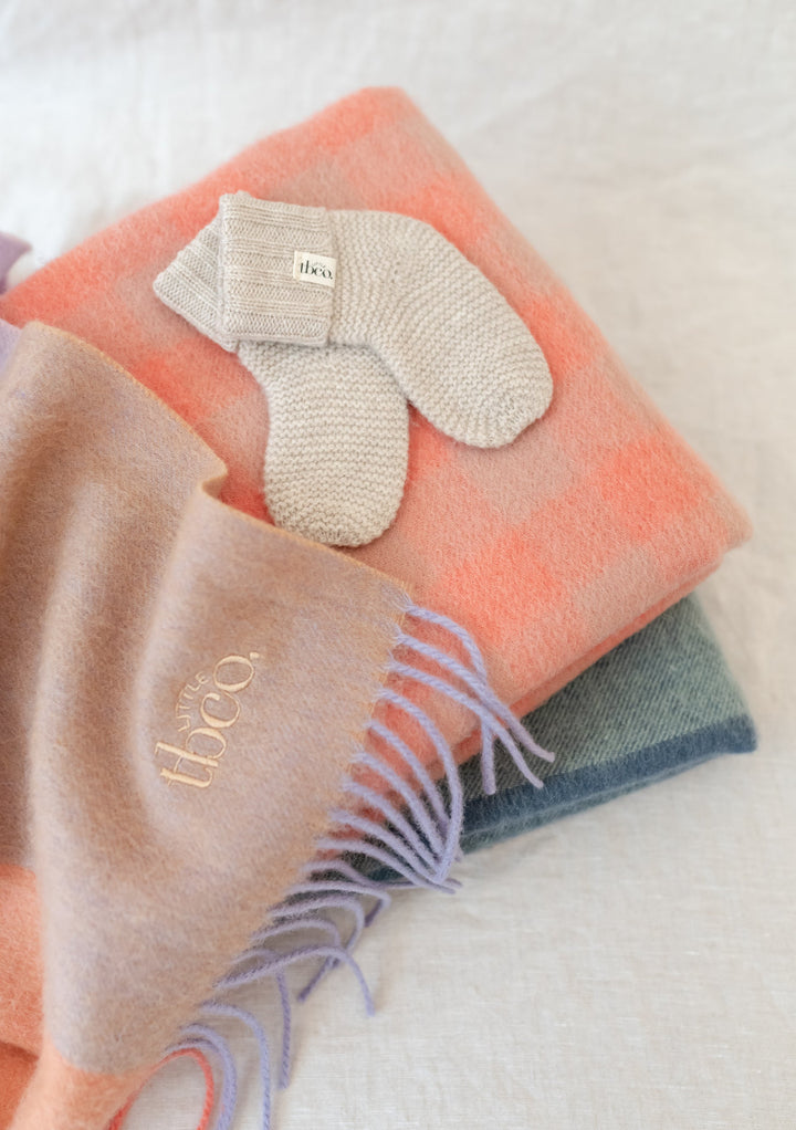 TBCo Merino Wool Baby Socks in Oatmeal Melange displayed on colourful wool blankets, showing knitted texture and brand label