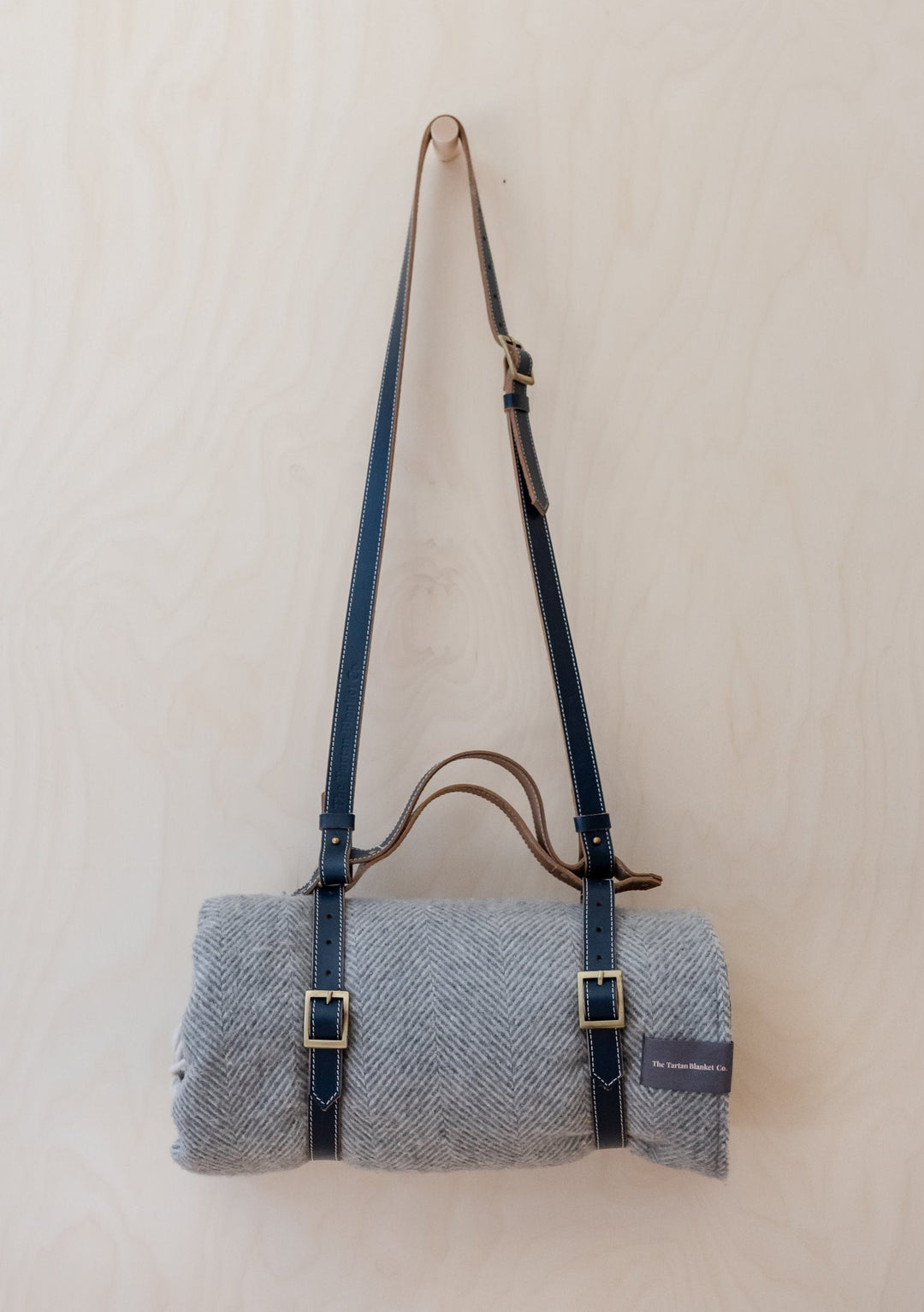 TBCo Leather Picnic Carrier with adjustable shoulder strap and brass buckles holding grey wool blanket against white background