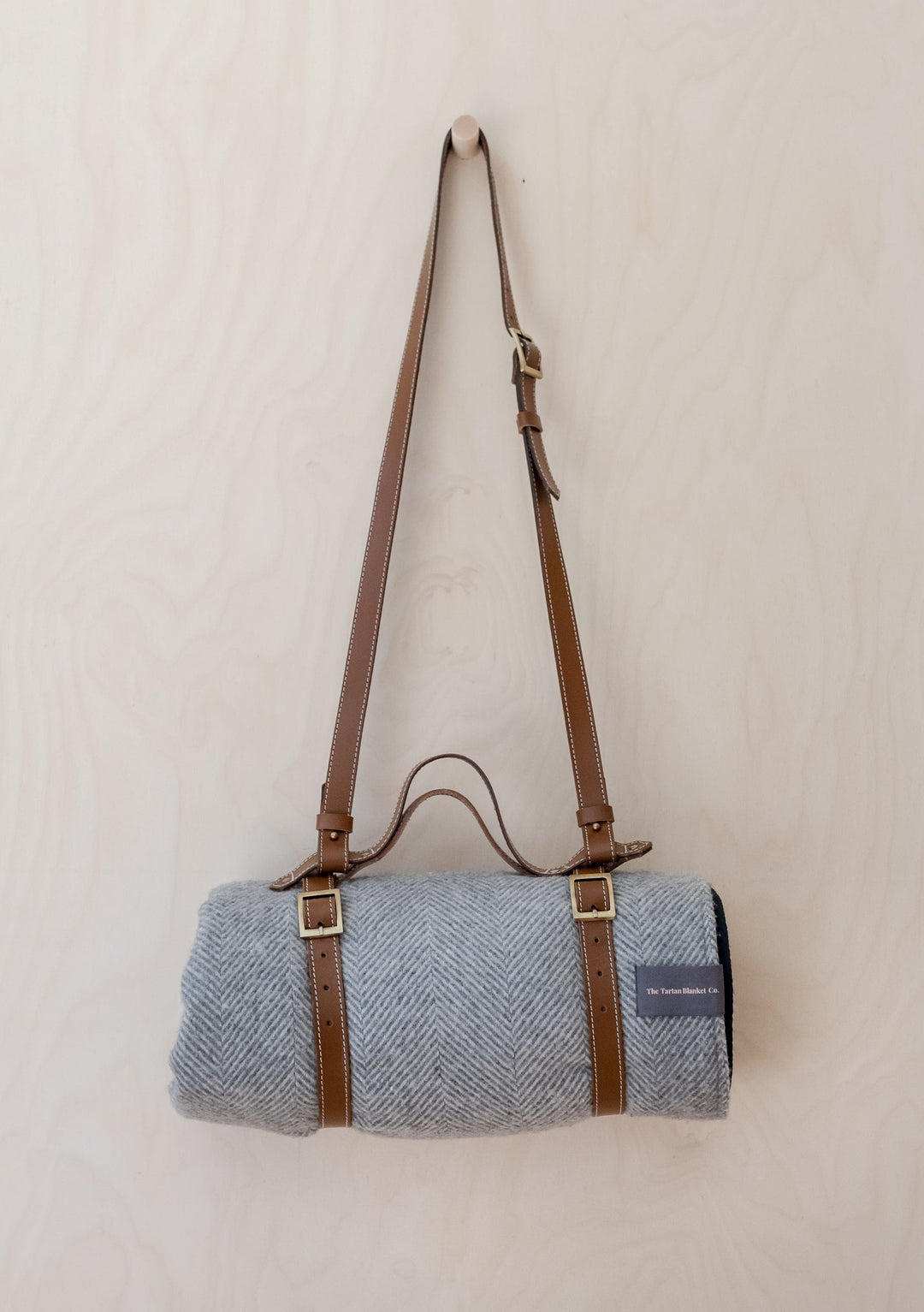 TBCo leather picnic carrier with adjustable shoulder strap shown with grey wool blanket and brass buckle details