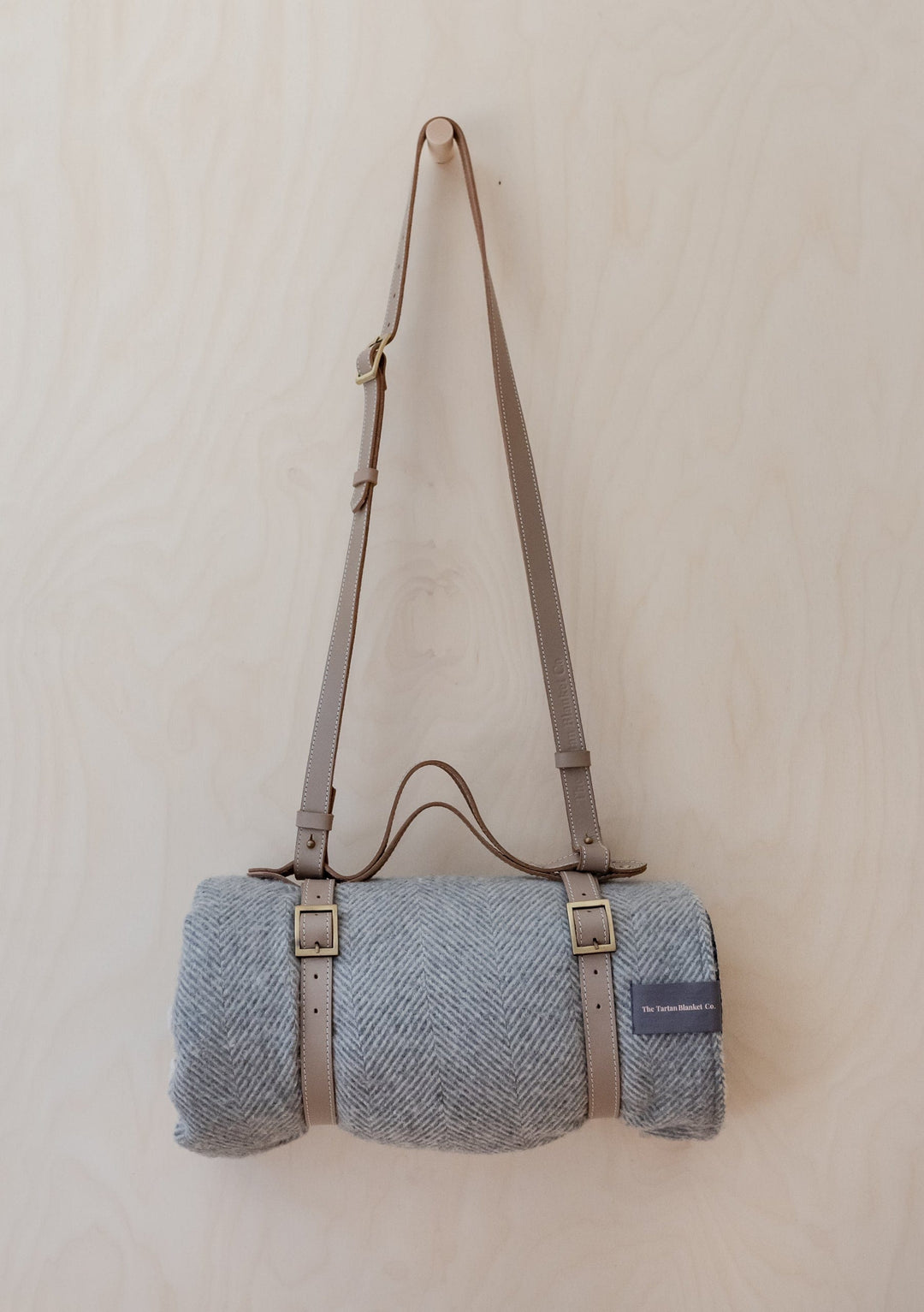 TBCo Leather Picnic Carrier with adjustable shoulder strap and brass buckles, shown with grey wool blanket rolled inside