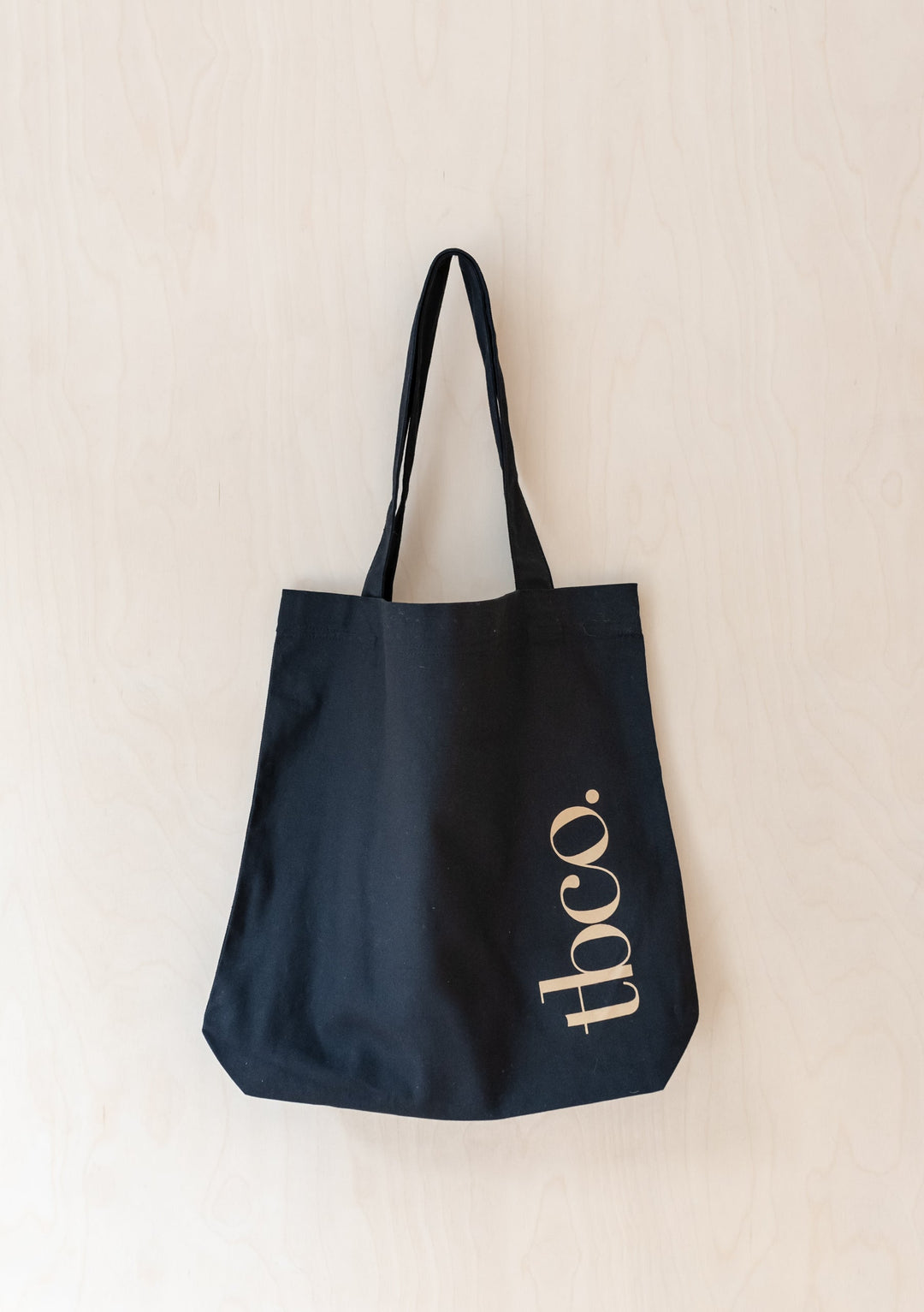 Black recycled cotton TBCo tote bag with gold logo displayed against neutral background, showcasing durable canvas construction