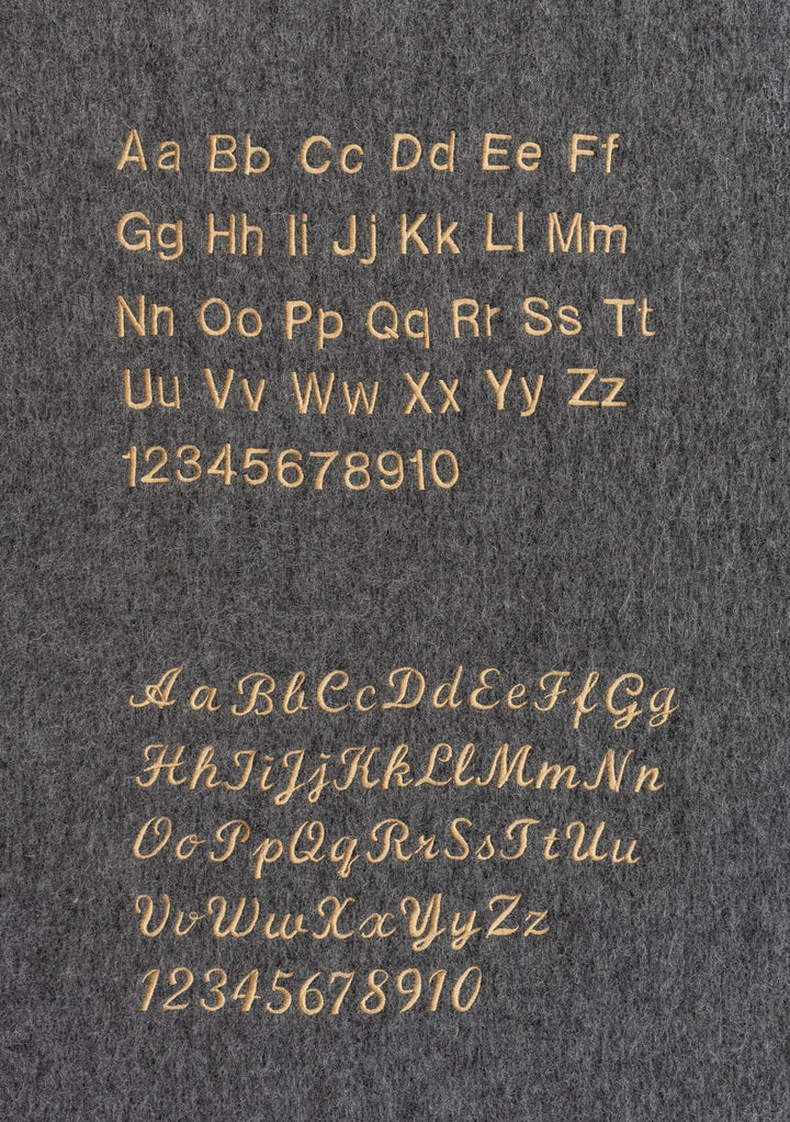 Embroidery examples on grey fabric showcasing TBCo Lambswool Oversized Scarf in Burgundy Wave lettering styles.