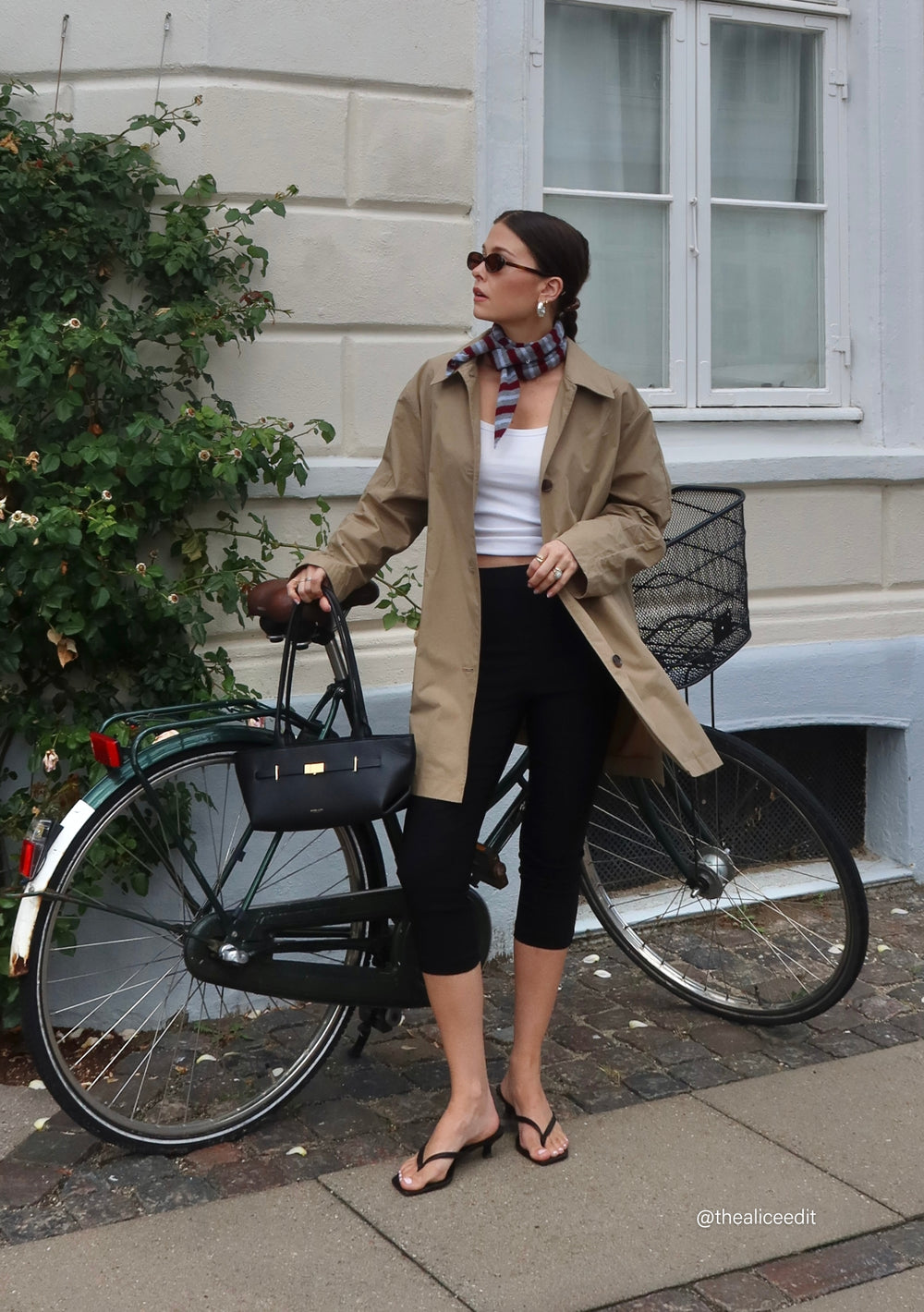 Woman wearing TBCo Merino Wool Neck Tie in Burgundy Stripe styled with trench coat and black cropped trousers by a bicycle