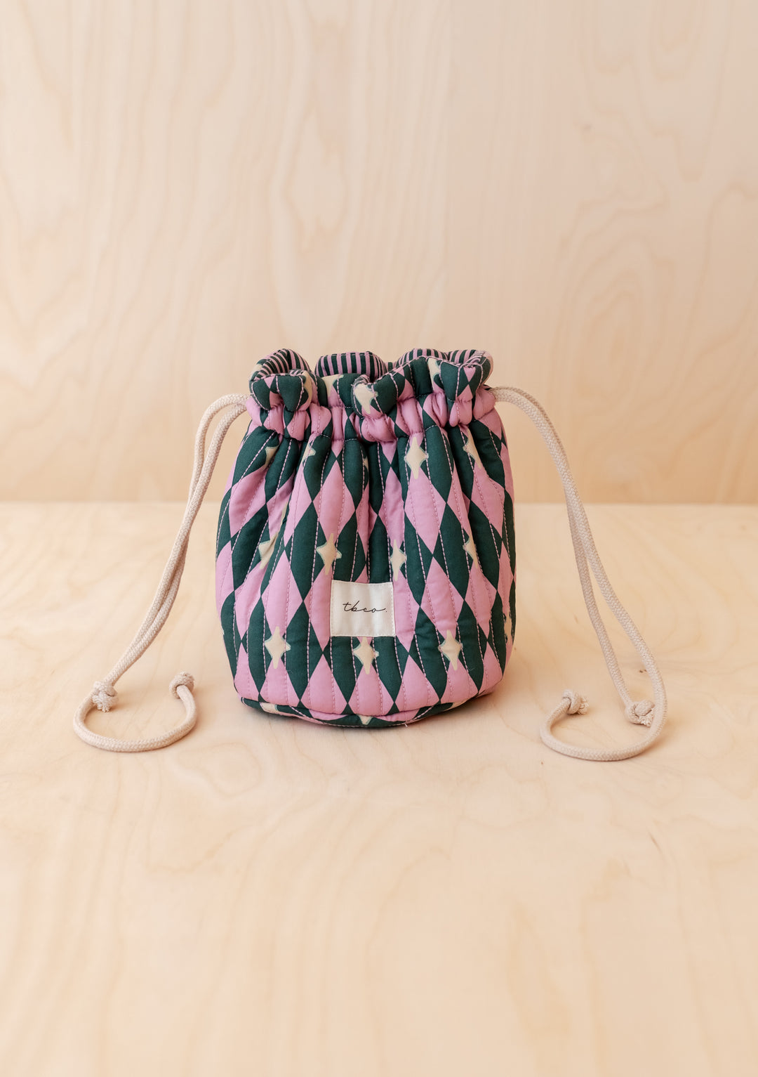 TBCo Cotton Wash Bag in Pink Harlequin pattern with drawstring, featuring a quilted design and fabric label tbco. on a light wood surface.