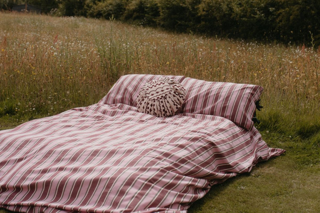 TBCo Cotton Pink Stripe Duvet Set on a bed with Cotton Pink Checkered Cushion lifestyle image set in a field with flowers surrounding