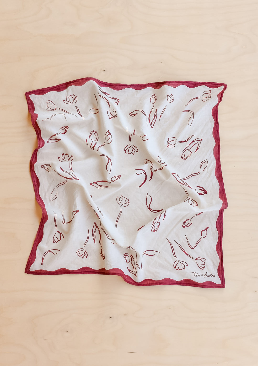 TBCo Harlie Briggs Artist Series Cotton Square Triangle Neck Scarf  with a floral white and red print laid flat on a wooden background