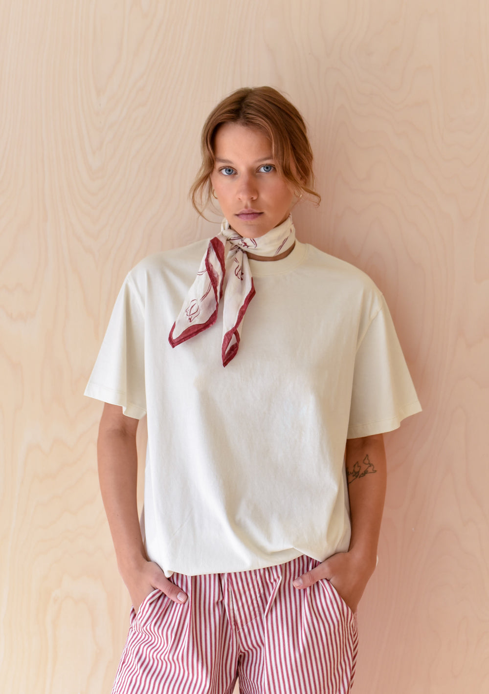 TBCo Chiara Perano Artist Series Cotton Square Triangle Neck Scarf with a red and white floral print and Cotton T-shirt worn by a model standing in front of a wooden background.