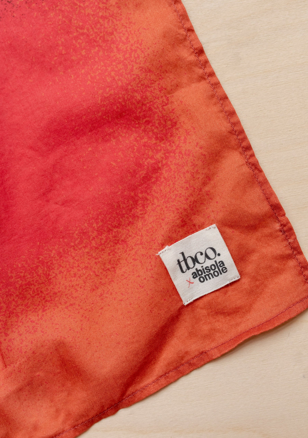 Close-up of Sample Sale TBCo x Abisola Omole Hues Cotton Scarf showing fabric texture and branded label on red-orange cotton material