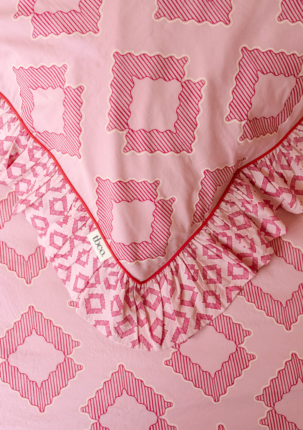 Close-up shot of TBCo Pair of Cotton Pillowcases in Pink Diamond showing red piping and ruffled edge, gallery 2 portrait