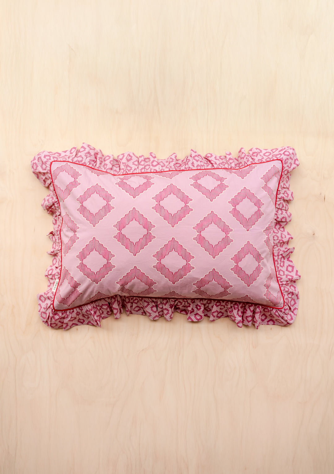 Pair of Cotton Pillowcases in Pink Diamond by TBCo featuring geometric pink shapes and ruffled edges on pale wood background