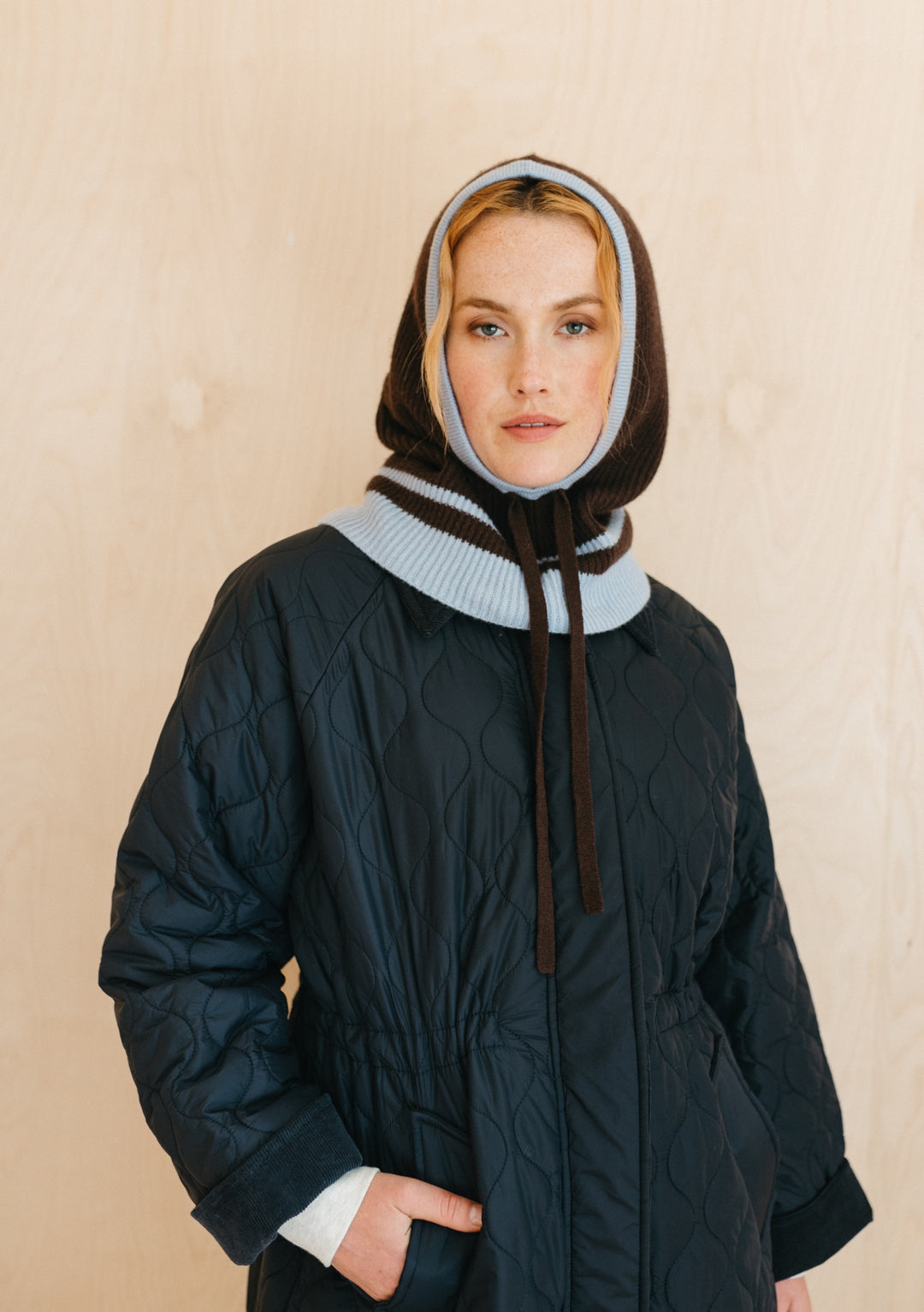 TBCo Merino Hood in Brown with ice blue trim shown with quilted winter coat, displaying hood's snug fit and versatile style