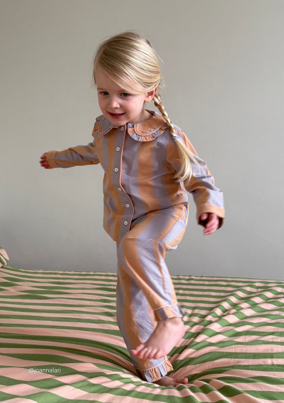 TBCo cotton kids pyjamas in orange and lilac stripes with ruffled collar, shown on striped bedding