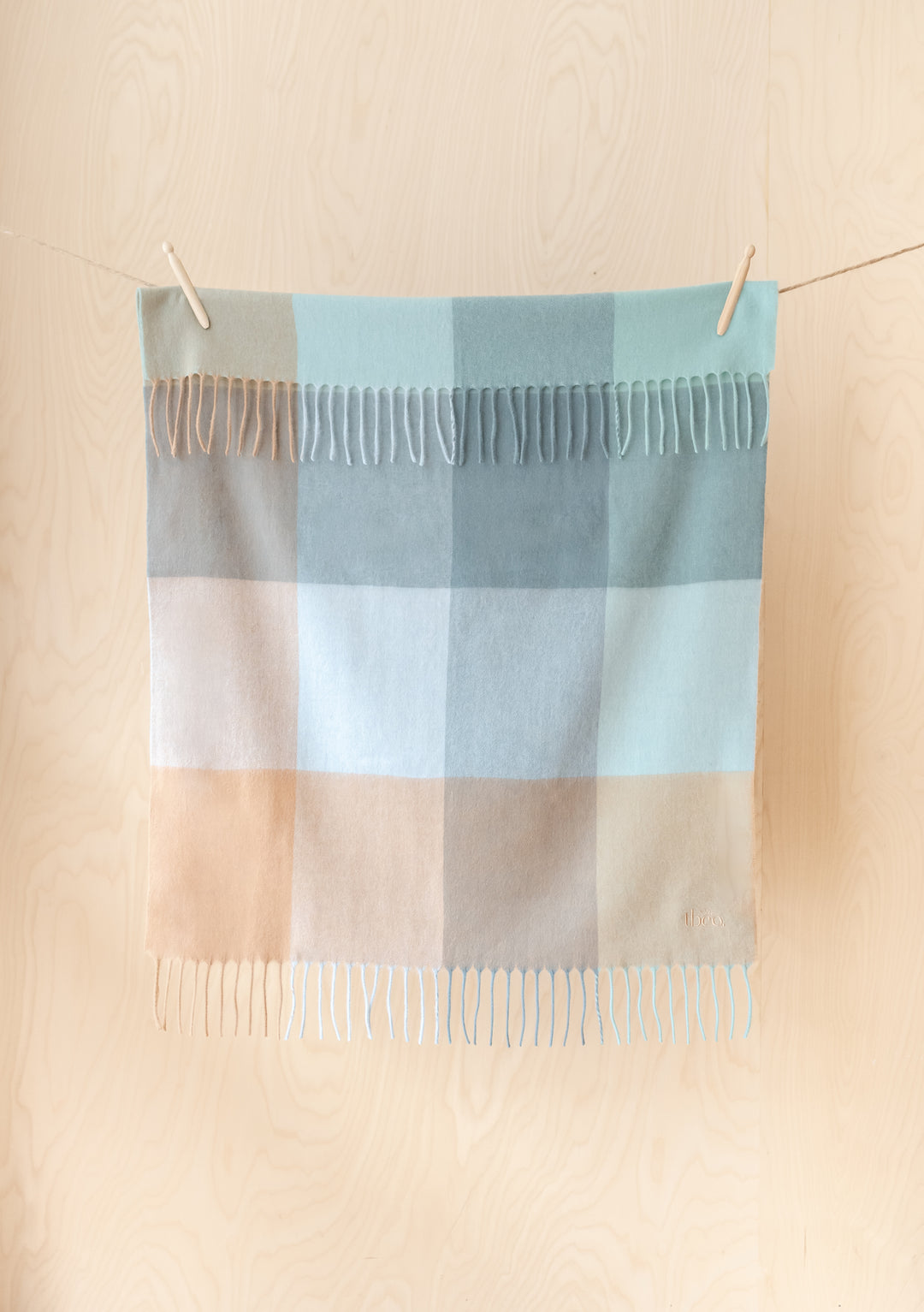 Lambswool Baby Blanket in Blue Block Check by TBCo hanging flat in portrait, showcasing soft colours and fringed edges.