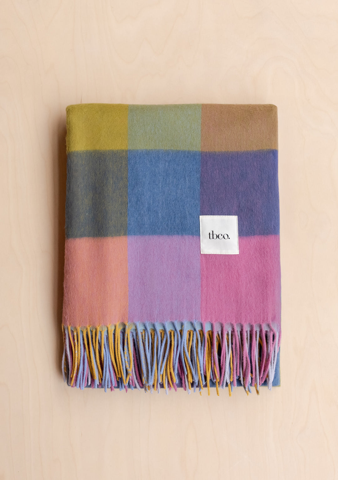Folded TBCo Lambswool Blanket in Pink Block Check showing soft fibres and fringed edges on a pale wood background