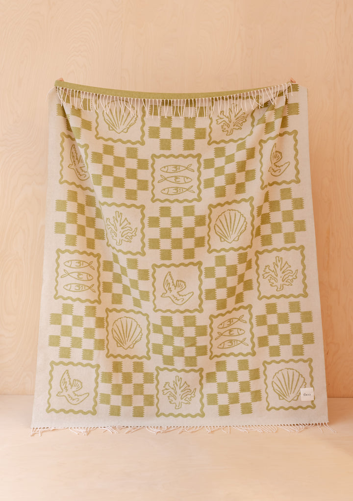 TBCo Lambswool Blanket in Green Motif hanging with checkered and coastal-themed illustrations in soft green tones