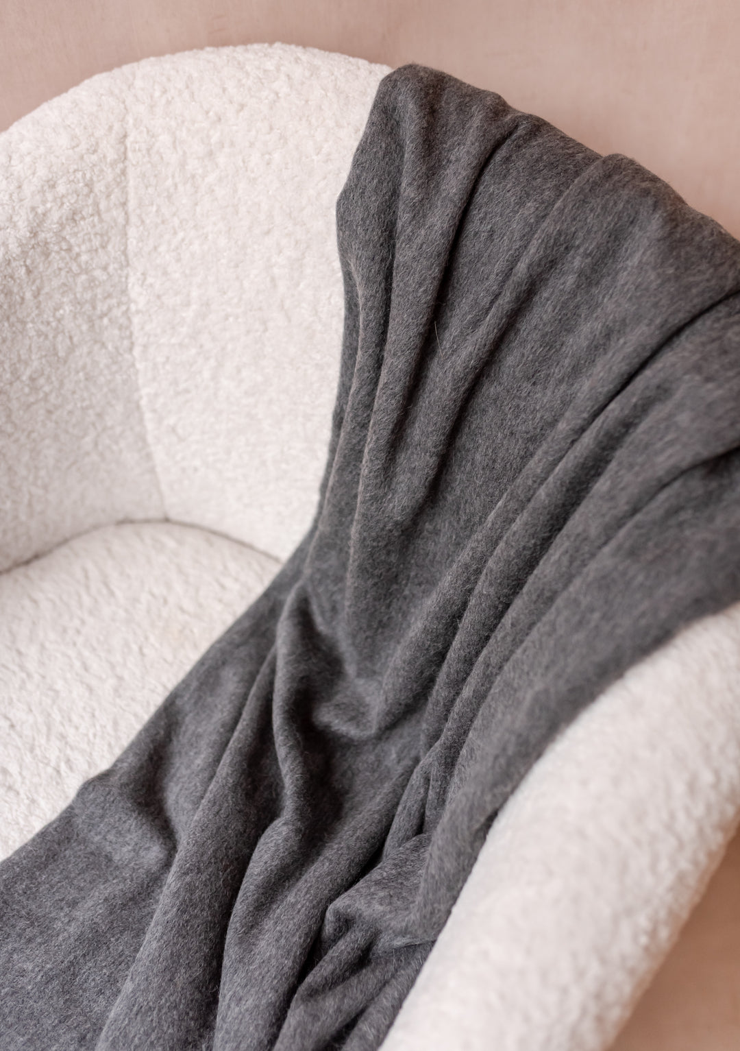 Soft TBCo Cashmere Small Blanket in Charcoal Melange draped over a cream boucle armchair with delicate fringe edges