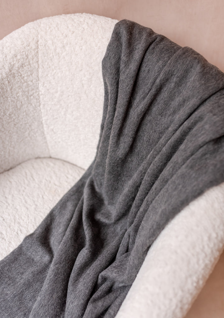Soft TBCo Cashmere Small Blanket in Charcoal Melange draped over a cream boucle armchair with delicate fringe edges