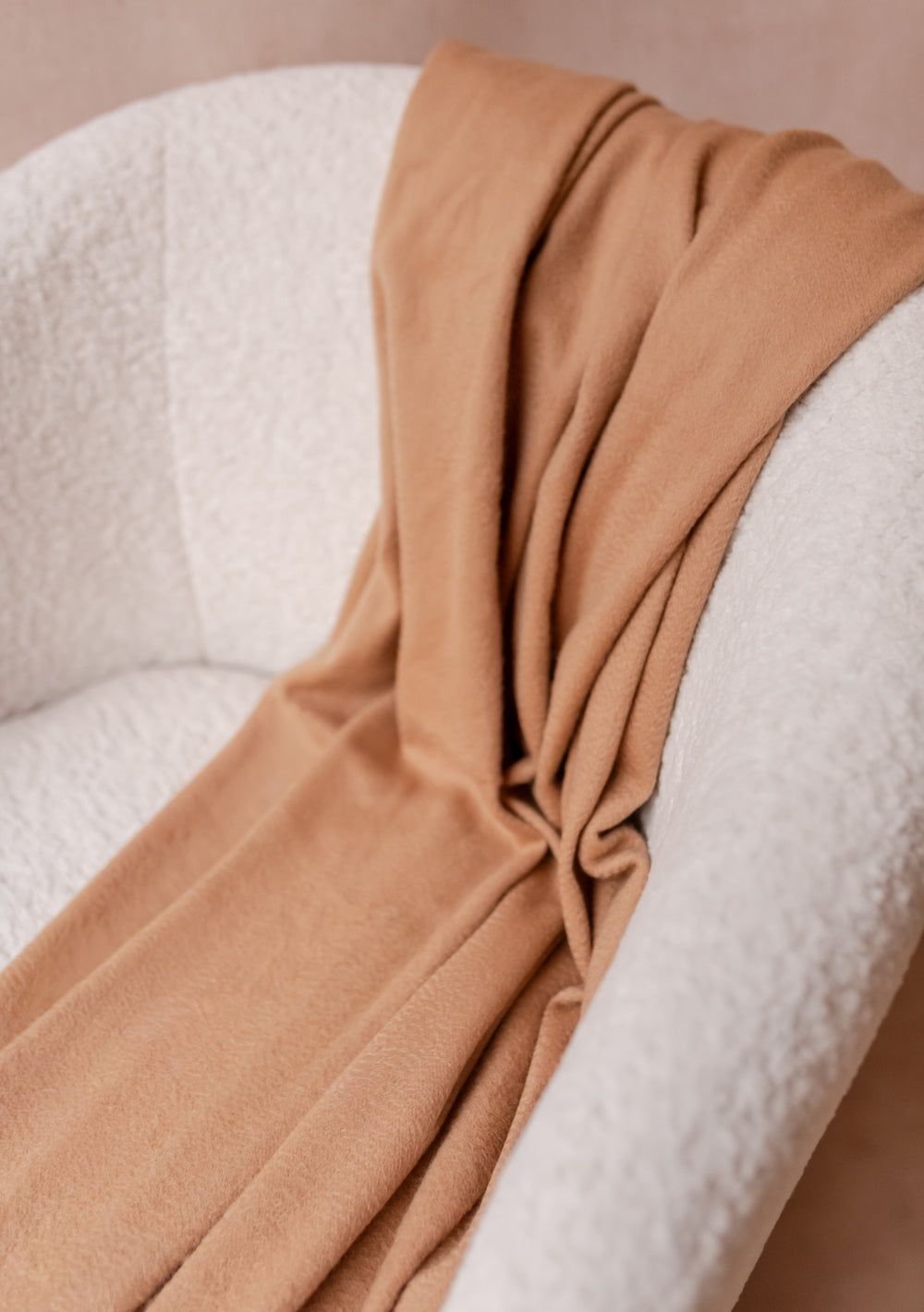 Cashmere Blanket in Camel by TBCo draped over a cream boucle armchair, showcasing soft texture and refined warmth.