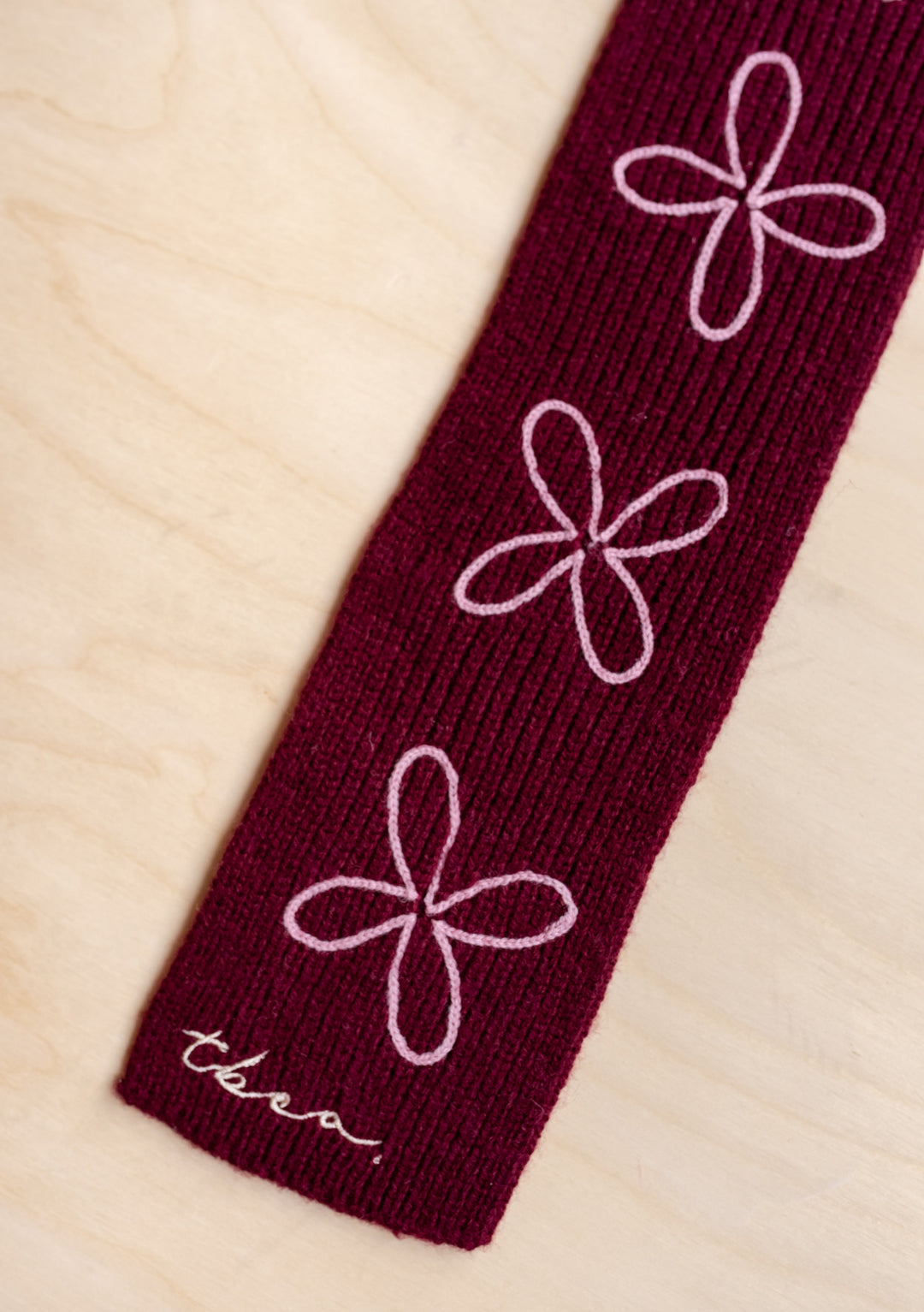 Close-up of TBCo Merino Wool Skinny Scarf in Burgundy Flora showing pale pink floral embroidery on soft ribbed fabric.