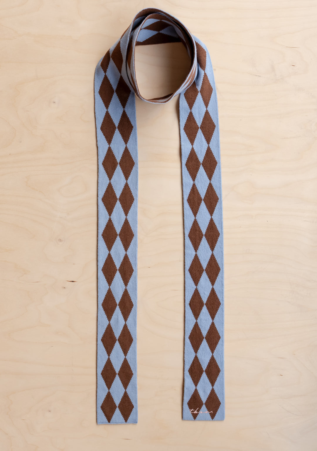 TBCo Merino Wool Skinny Scarf in Brown Harlequin with blue and brown diamond pattern laid flat on light wood surface
