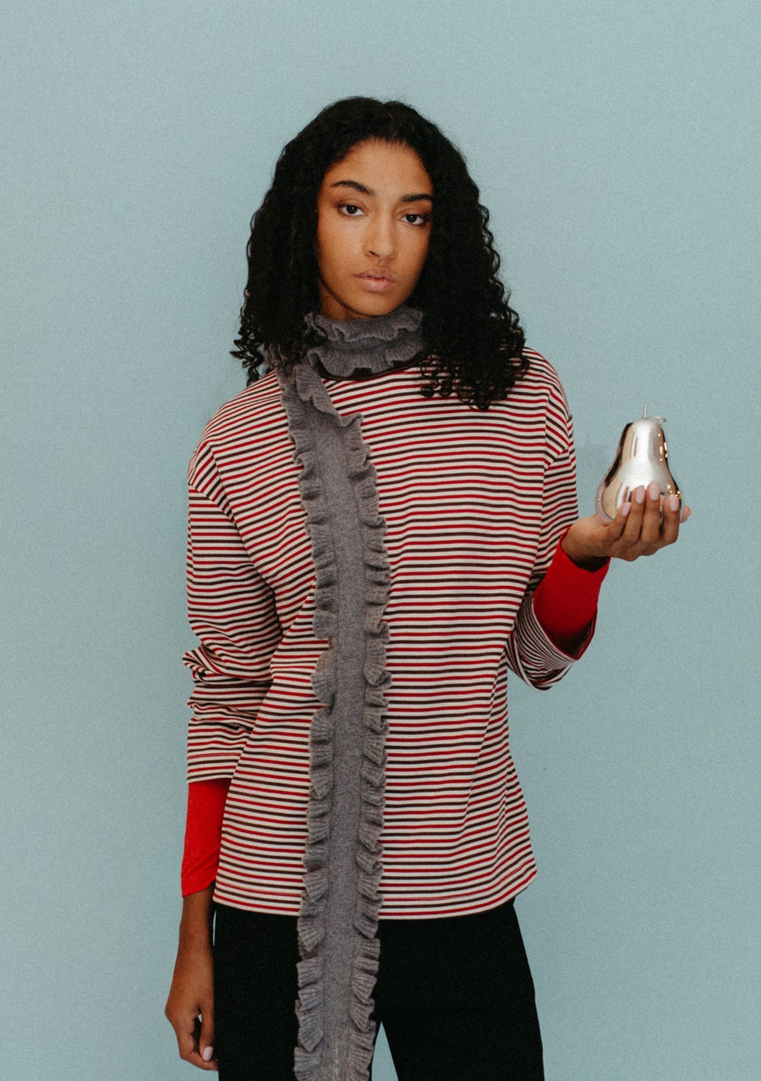 Model wearing TBCo Merino Wool Skinny Scarf in Grey Ruffle with ruffled trim over striped top against pale blue background