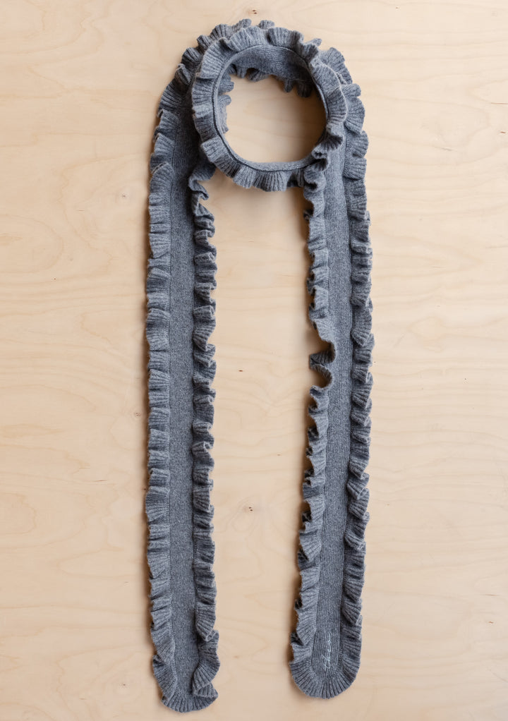 TBCo Merino Wool Skinny Scarf in Grey Ruffle laid flat on wooden surface showing ruffled edges and soft texture