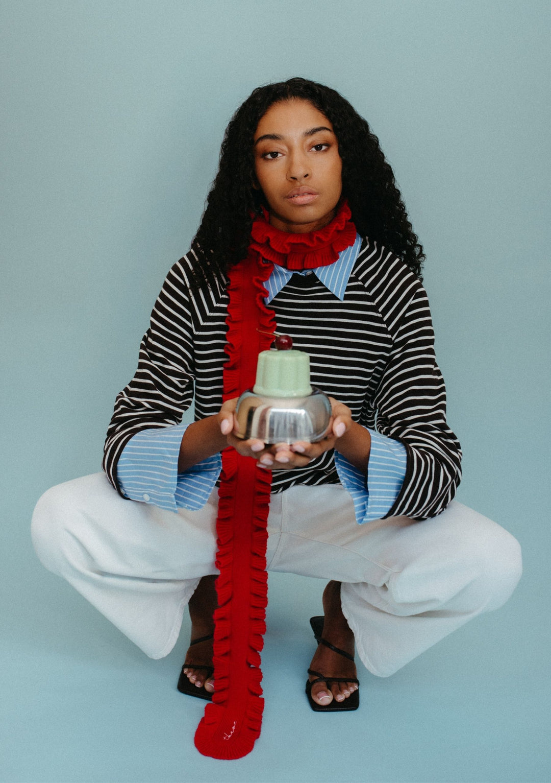 Model wearing TBCo Merino Wool Skinny Scarf in Red Ruffle with ruffled trim styled over striped top and white trousers