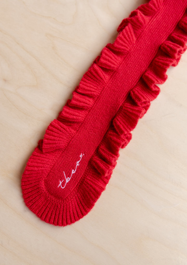 Close-up of TBCo Merino Wool Skinny Scarf in Red Ruffle showing ribbed texture and embroidered detail on light wood background