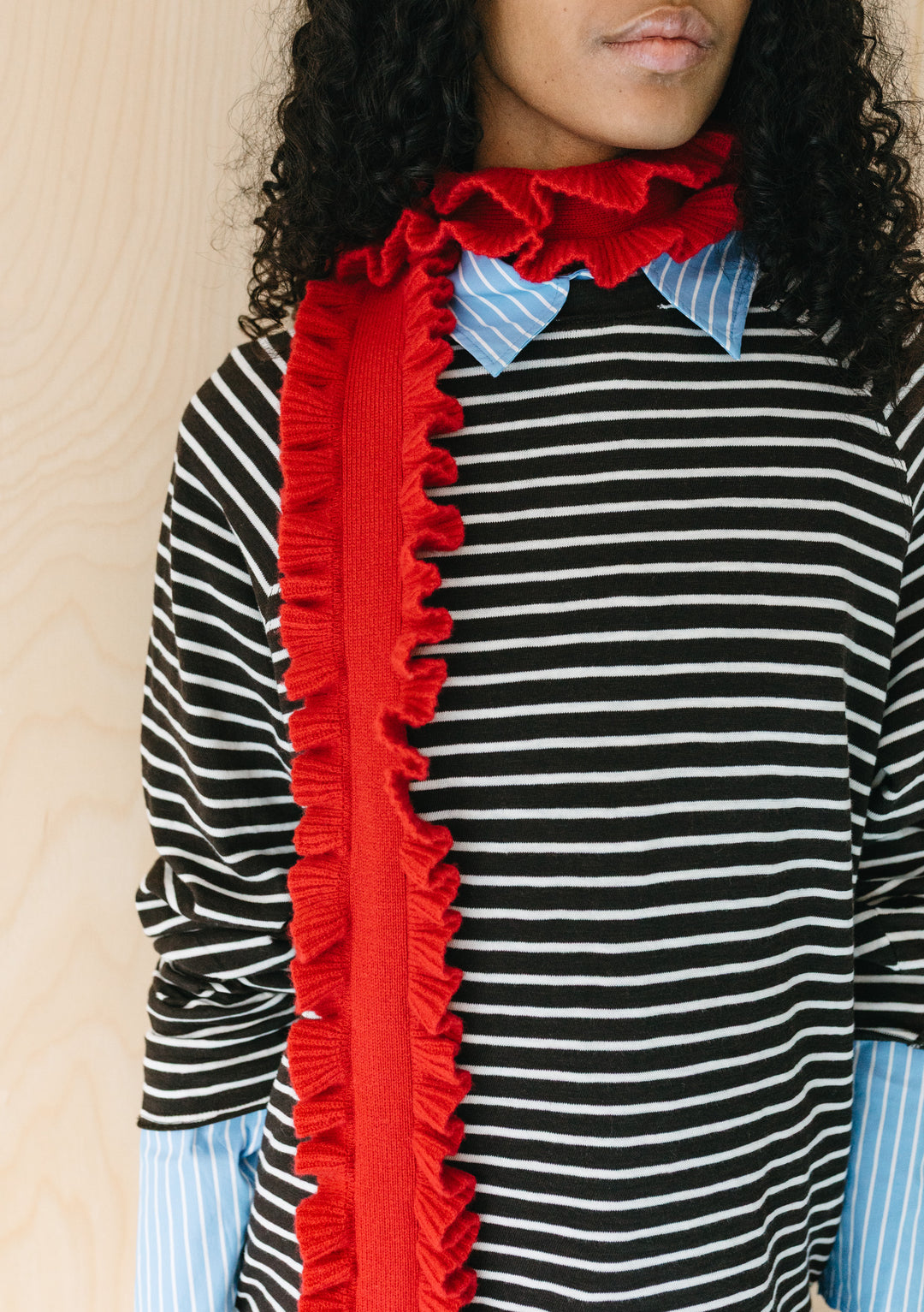 Model wearing TBCo Merino Wool Skinny Scarf in Red Ruffle with textured ruffled trim against a striped shirt background