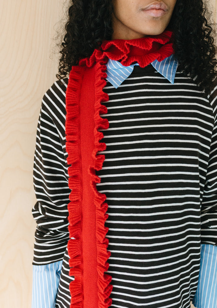 Model wearing TBCo Merino Wool Skinny Scarf in Red Ruffle with textured ruffled trim against a striped shirt background