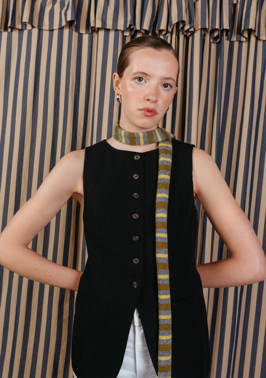 Model wearing a TBCo Merino Wool Neck Tie in Green Stripe, styled over a black waist-coat and light jeans, showcasing its subtle elegance and transitional-inspired design.