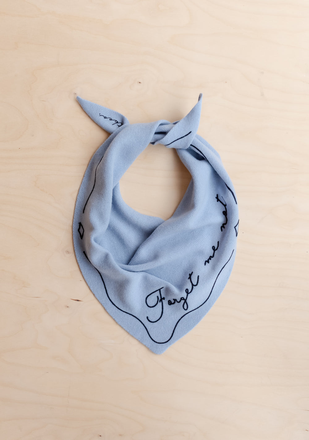 TBCo Merino Wool Triangle Scarf in Forget Me Not in pale blue with black embroidered detail laid flat on wooden background