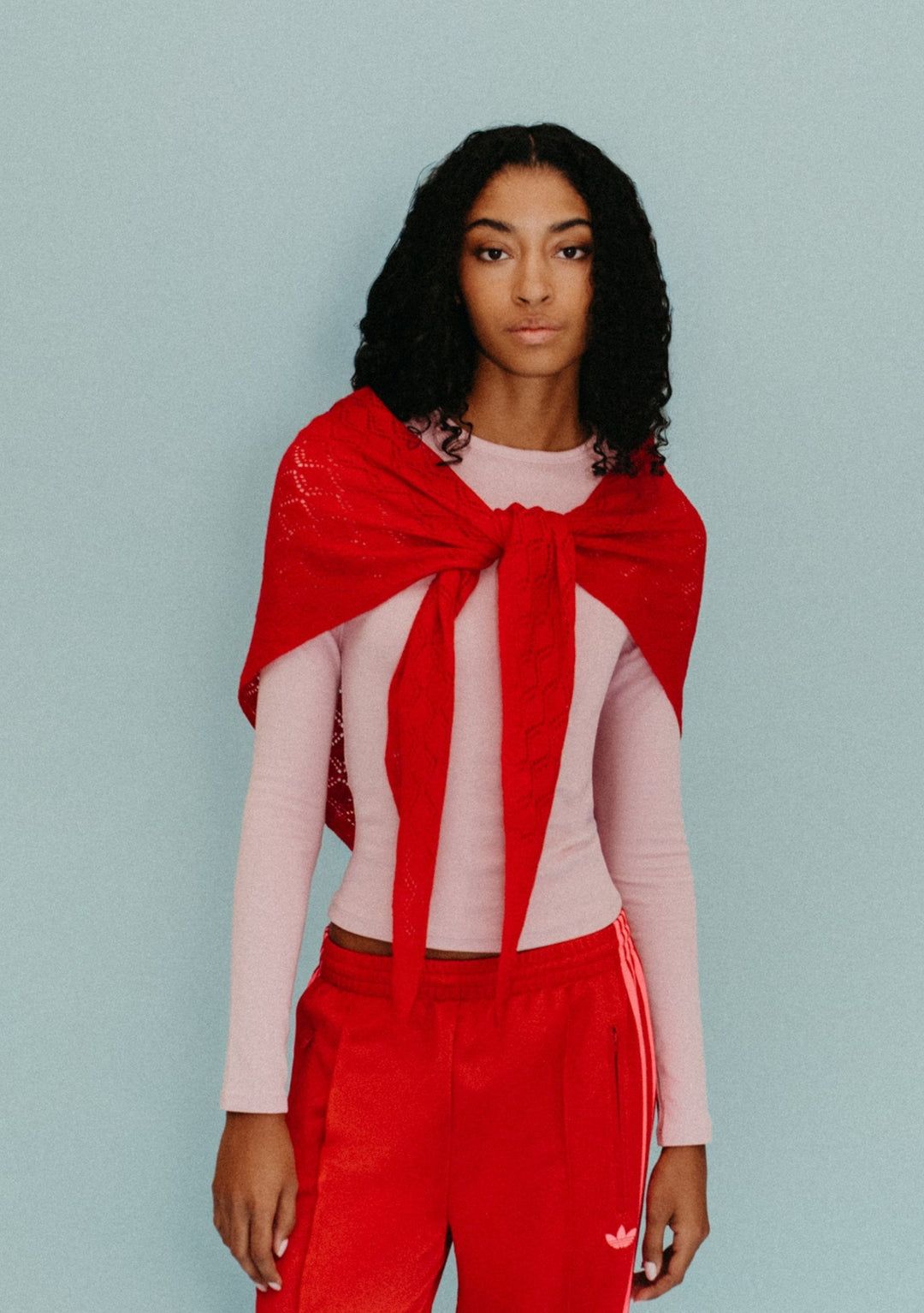 Model wearing TBCo Large Merino Wool Triangle Scarf in Red Pointelle tied loosely over a pale pink top