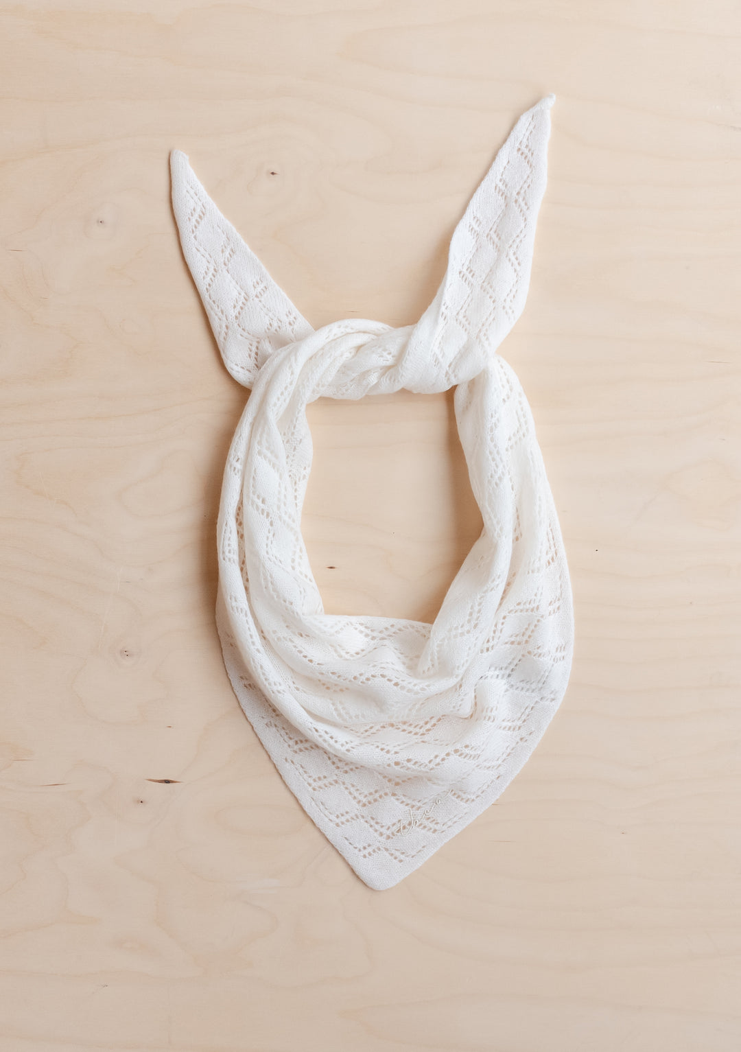 TBCo Merino Wool Triangle Scarf in White Pointelle knitted with delicate diamond pattern laid flat on light wood surface