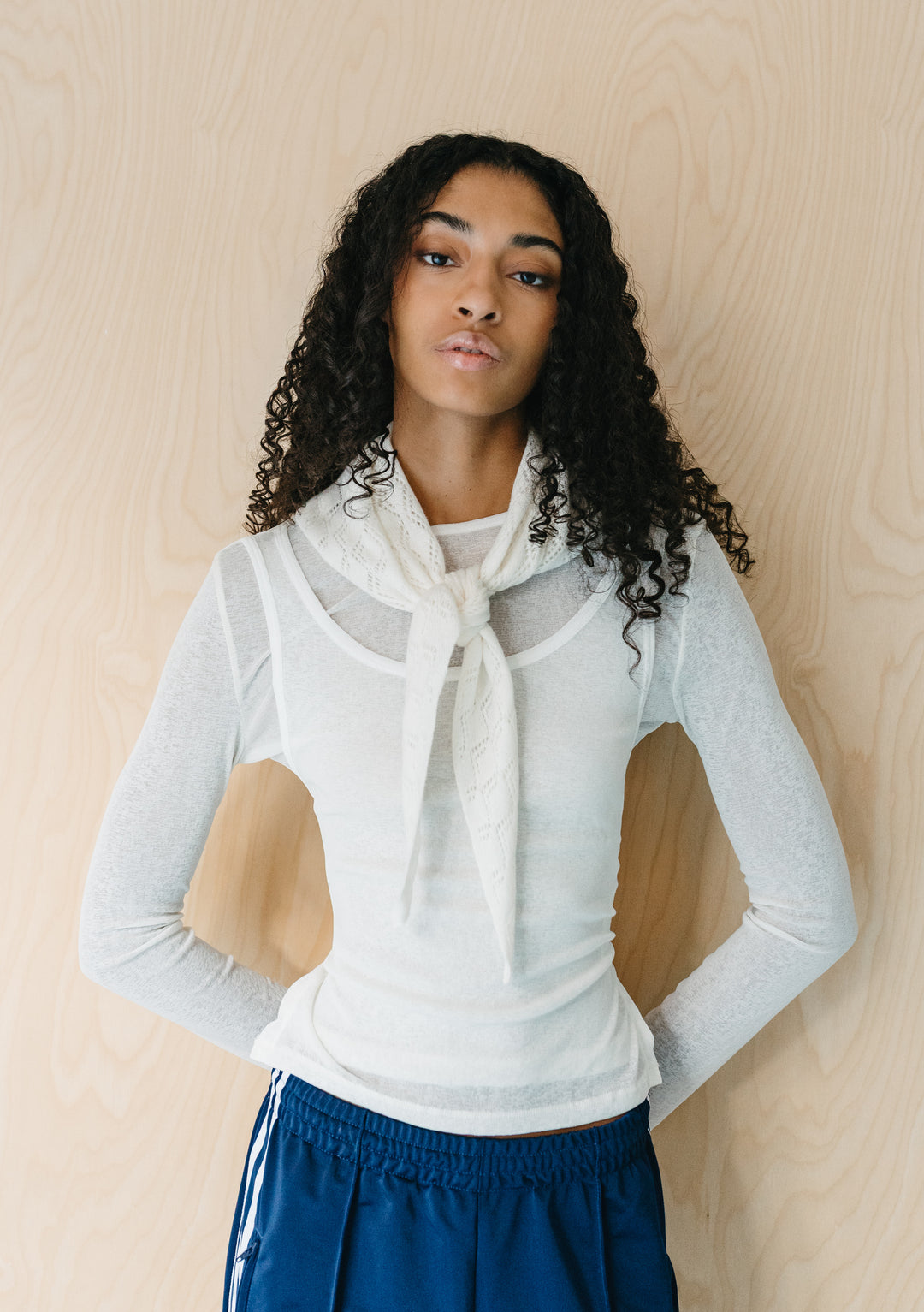 Model wearing TBCo Merino Wool Triangle Scarf in White Pointelle tied at neck with sheer white top and blue trousers