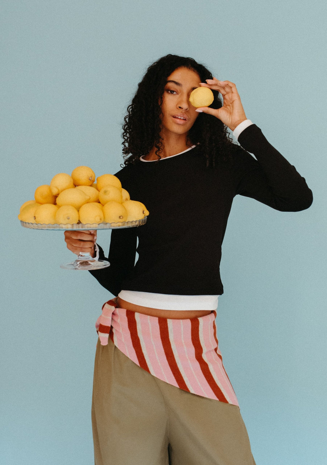 Model wearing TBCo Merino Wool Triangle Scarf in Pink & Rust Stripe tied at waist with relaxed trousers and black top