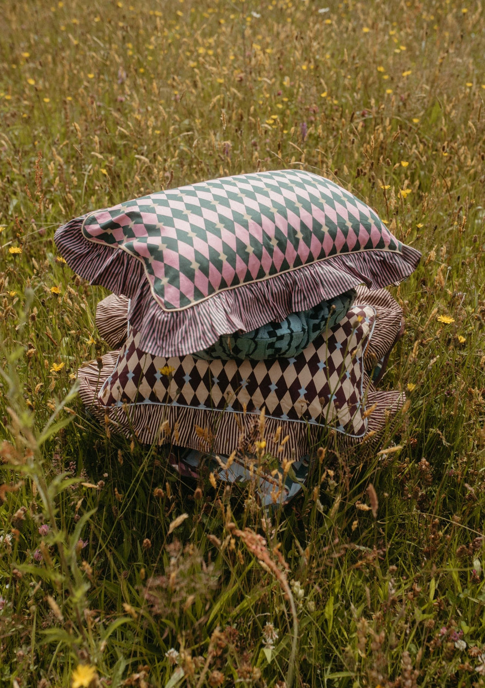 Stack of patterned cushions in a wildflower meadow showcasing the Mix & Match Cushion Set by TBCo with sustainable cotton covers